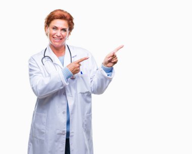 Gülümseyen ve iki elleri ve parmakları ile tarafına işaret kamera bakarak izole arka plan üzerinde tıbbi üniforma giyen üst düzey beyaz doktor kadın.