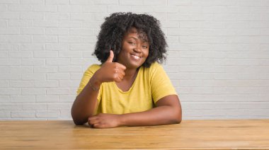Evde masaya oturan genç Afro-Amerikan kadın hareketi el ile mutlu yaşasın yapıyor. Kameraya bakarak başarı gösteren ile ifade onaylama.