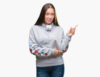 Yüzünde kocaman bir gülümseme ile izole arka plan üzerinde kulaklık giyen genç güzel beyaz öğrenci kadın kameraya bakarak yan el ve parmak ile işaret.