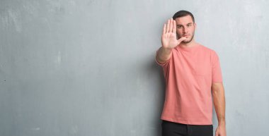 Beyaz delikanlı dur yapıyor gri grunge duvarın üzerinden elin avuç ile şarkı. Negatif ve ciddi bir jest yüz ifadesiyle uyarı.