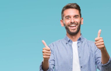 Yakışıklı delikanlı izole arka plan başarı işareti el ile pozitif jest yapıyor üzerinde beyaz t-shirt giyen başparmak gülümseyen ve mutlu. Neşeli bir ifadeyle, kazanan jest kameraya bakıyor.