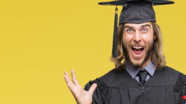 Genç yakışıklı lisansüstü adam uzun saçlı derecesi izole arka plan üzerinde çok mutlu ve heyecanlı, kocaman bir gülümseme ile çığlık ve ellerini kaldırdı kazanan ifade kutluyor zafer tutarak