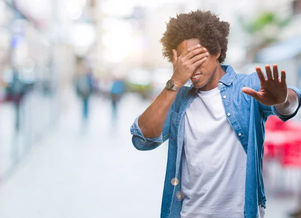 Afro american man over isolated background covering eyes with hands and doing stop gesture with sad and fear expression. Embarrassed and negative concept.