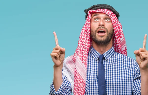 Young handsome arabian business man wearing keffiyeh over isolated background amazed and surprised looking up and pointing with fingers and raised arms.