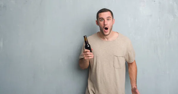 Joven Hombre Caucásico Sobre Pared Grunge Gris Sosteniendo Cerveza Botella —  Fotos de Stock