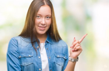 Yüzünde kocaman bir gülümseme ile izole arka plan üzerinde genç Kafkas güzel kadın kameraya bakarak yan el ve parmak ile işaret.