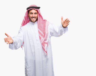 Sarılmak için kollarını açarak gülümseyerek kameraya bakarak izole arka plan üzerinde keffiyeh giyen genç yakışıklı adam. Neşeli ifade kucaklayan mutluluk.