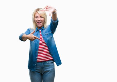 Elle yapma çerçeve ve parmakları ile mutlu yüz gülümseyen izole arka plan üzerinde kot ceket giyen genç güzel sarışın kadın. Yaratıcılık ve Fotoğrafçılık kavramı.