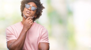 Afro Amerikalı adam çene düşünme hakkında soru, dalgın ifade üzerine el ile izole arka plan üzerinde güneş gözlüğü takıyor. Düşünceli yüzüyle gülümsüyor. Şüphe kavramı.