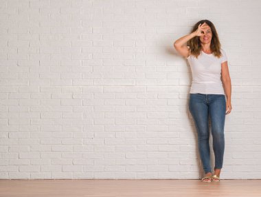 Orta yaş İspanyol kadın mutlu yüz el parmaklarının arasından seyir göz üzerinde ok işaretiyle yapıyor gülümseyen ile beyaz tuğla duvarı ayakta