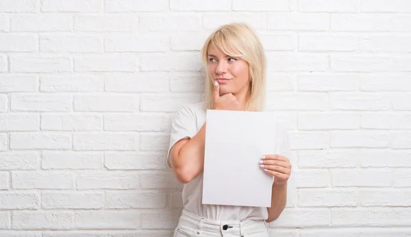 Mujer Caucásica Adulta Sobre Pared Ladrillo Blanco Sosteniendo Hoja Papel —  Fotos de Stock