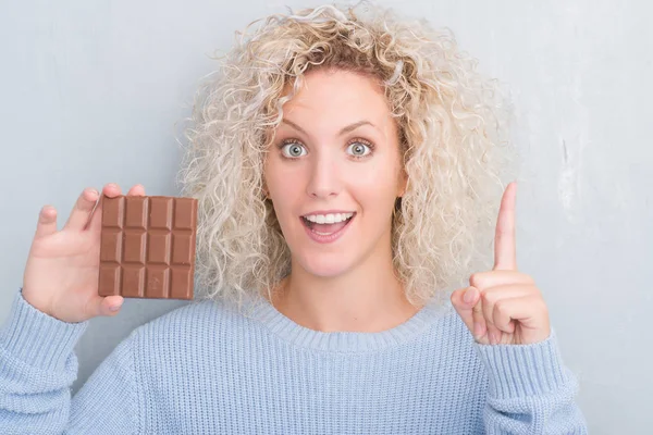 Joven Mujer Rubia Sobre Pared Gris Grunge Comiendo Barra Chocolate —  Fotos de Stock