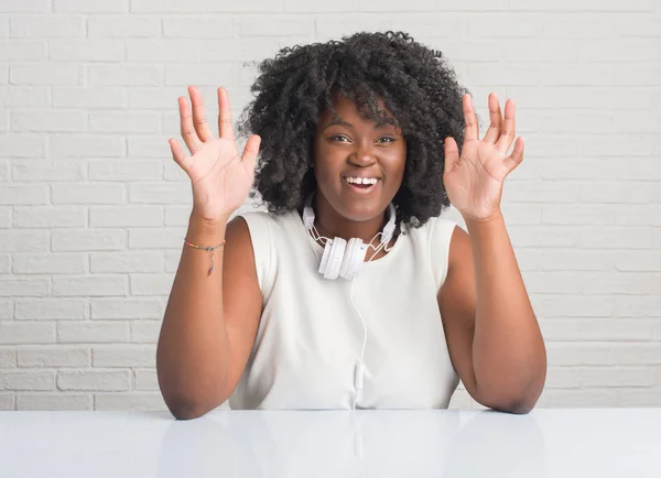 Young african american woman sitting on the table wearing headphones celebrating crazy and amazed for success with arms raised and open eyes screaming excited. Winner concept