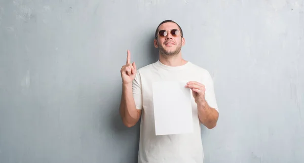 Joven Hombre Caucásico Sobre Pared Grunge Gris Sosteniendo Papel Blanco — Foto de Stock