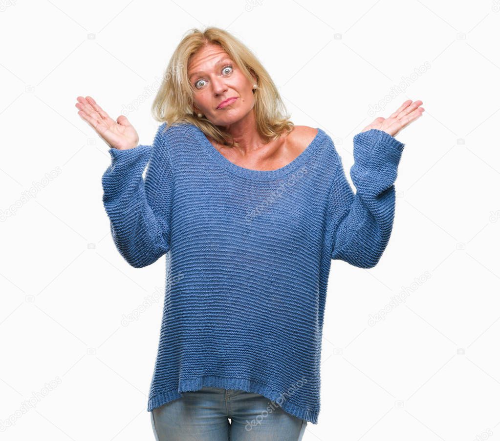 Middle age blonde woman wearing winter sweater over isolated background clueless and confused expression with arms and hands raised. Doubt concept.