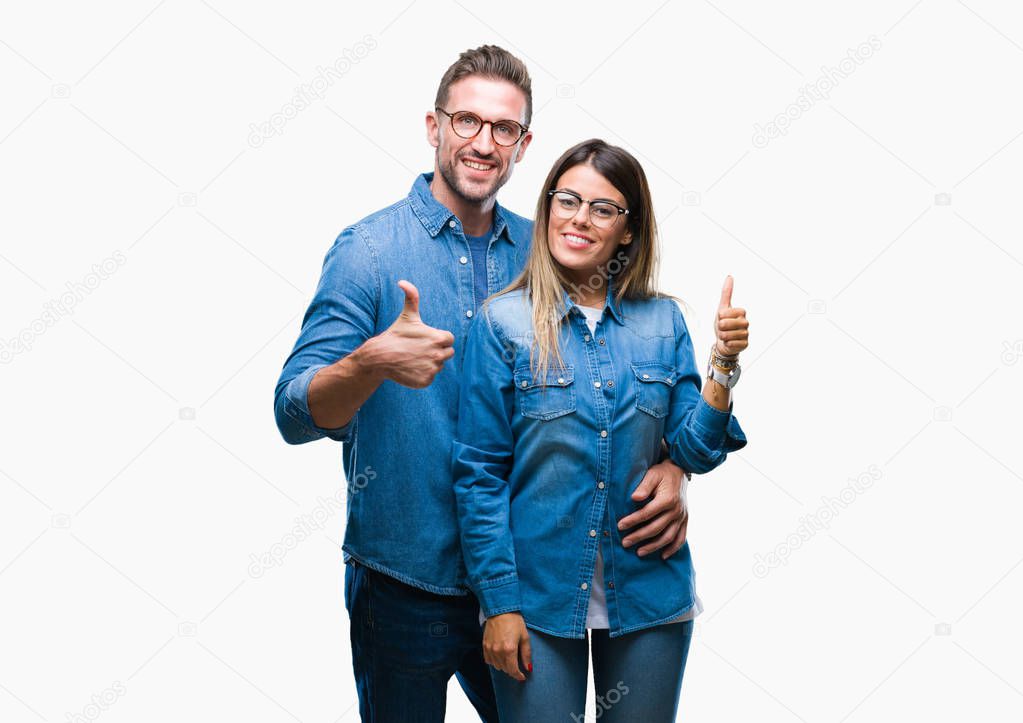 Young couple in love wearing glasses over isolated background doing happy thumbs up gesture with hand. Approving expression looking at the camera with showing success.