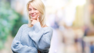 Emin çapraz kollar ve çeneme kaldırdı el ile gülümseme ile kameraya bakarak izole arka plan üzerinde kış kazak giyen genç güzel sarışın kadın. Pozitif düşünce.