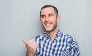 İşaret ve başparmak kadar mutlu yüz gülümseyen tarafı ile gösterilen gri grunge duvarın üzerinden beyaz delikanlı