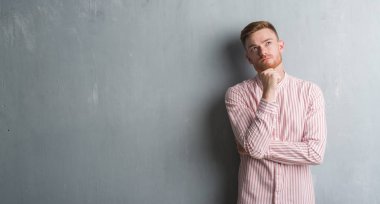 Gri grunge duvar ciddi bir yüz düşünme hakkında soru, çok karışık fikir genç Kızıl saçlı adam