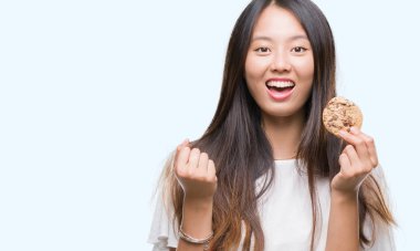 Duygu tezahürat Genç Asyalı kadın gurur çığlık ve zafer ve başarı çok heyecanlı, kutluyor izole arka plan üzerinde çikolatalı kurabiye yemek