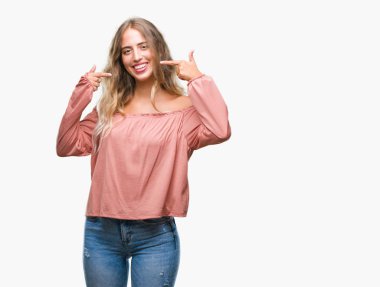 Güzel sarışın genç kadın kendine güvenen gösterilen ve işaret parmakları diş ve ağız ile gülümseyen izole arka plan üzerinde. Sağlık kavramı.