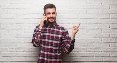 Üzerinde telefon duran beyaz tuğla konuşan genç yetişkin adam duvar çok mutlu el ve parmak ile işaret yan