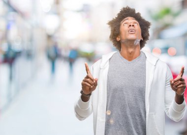 Afro Amerikalı adam kazak giyiyor izole arka plan üzerinde hayret ve yukarıya bakıp parmakları ile işaret şaşırttı ve silah kaldırdı.