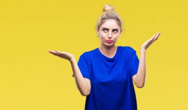 İzole arka plan clueless ve şaşkın bir ifadeyle kollar ve eller kaldırdı üzerinde mavi t-shirt giyen genç güzel sarışın ve mavi gözlü kadın. Şüphe kavramı.