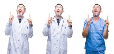 Kolaj yakışıklı üst düzey ağarmış Doktor adam cerrah üniforması izole arka plan üzerinde bir hayran ve yukarıya bakıyor ve parmakları ile işaret ve silah kaldırdı şaşırttı.