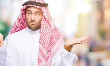 Keffiyeh izole arka plan clueless ve şaşkın bir ifadeyle kollar ve eller kaldırdı üzerinde giyen genç yakışıklı adam. Şüphe kavramı.