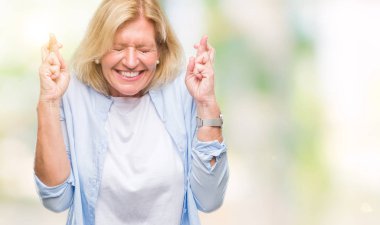 Orta yaş sarışın kadın geçiş parmakları umut ve gözler gülümseyen izole arka plan yüzünden kapalı. Şans ve batıl kavramı.