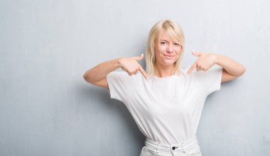 Yüzünde gülümseme ile kendinden emin görünüyorsun, kendini gururlu ve mutlu parmakları ile işaret grunge gri duvar yetişkin beyaz kadın.