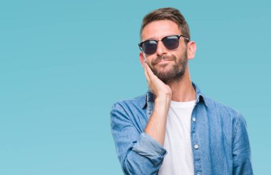 Genç yakışıklı adam çene düşünme hakkında soru, dalgın ifade üzerine el ile izole arka plan üzerinde güneş gözlüğü takıyor. Düşünceli yüzüyle gülümsüyor. Şüphe kavramı.