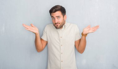 Yaz gömlek clueless ve şaşkın bir ifadeyle kollar ve eller kaldırdı giyen gri grunge duvarın üzerinden yakışıklı genç adam. Şüphe kavramı.