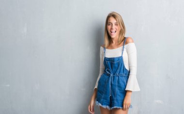 Grunge gri duvar seksi bir ifadeyle, neşeli ve mutlu yüzünü kameraya bakarak göz kırpıyor üzerinde duran güzel genç kadın.