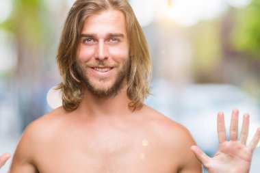 Genç yakışıklı gömleksiz adam uzun saçlı seksi vücut gösterilen ve parmakları ile işaret izole arka plan üzerinde gösterilen kendinden emin ve mutlu gülümseyerek süre on numara.