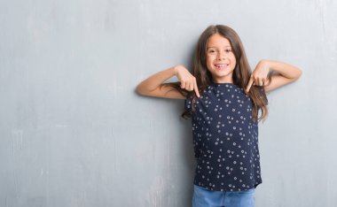 Genç İspanyol çocuğun yüzünde gülümseme ile kendinden emin görünüyorsun, kendini gururlu ve mutlu parmakları ile işaret grunge gri duvarın üzerinden.