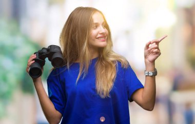 Genç güzel sarışın kadın izole arka tarafına el ve parmak ile işaret çok mutlu üzerinde dürbün ile seyir