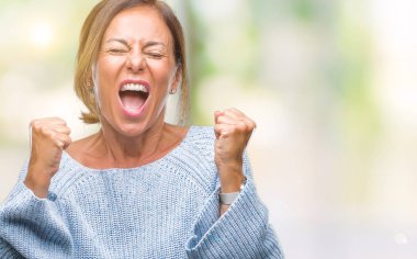 Üzerinde kış kazak giyen orta yaş üst düzey İspanyol kadın gülümseyerek ve başarı için çığlık arka plan çok mutlu ve heyecanlı kaldırdı, silah ile kazanan jest yapıyor izole. Kutlama kavramı.