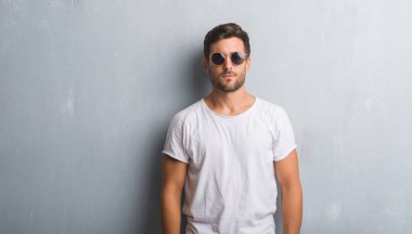 Yüzünde ciddi bir ifade ile güneş gözlüğü takıyor gri grunge duvarın üzerinden yakışıklı genç adam. Basit ve doğal kameraya bakıyor.