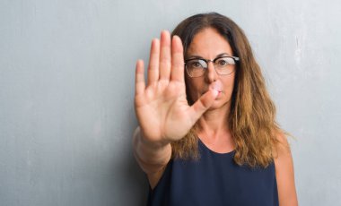 Gri duvar açık eliyle dur işareti ile ciddi ve kendine güvenen ifade, savunma jest yapıyor gözlük takan orta yaş İspanyol kadın
