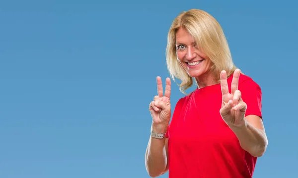 勝利のサインをやって指を表示するカメラを笑みを浮かべて隔離された背景に中年の金髪の女性 — ストック写真