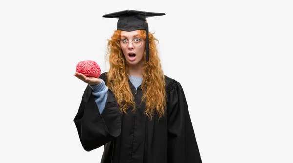 Jovem Estudante Ruiva Vestindo Uniforme Graduado Segurando Cérebro Assustado Choque — Fotografia de Stock