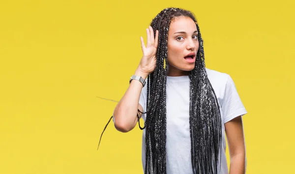 Young braided hair african american girl over isolated background smiling with hand over ear listening an hearing to rumor or gossip. Deafness concept.