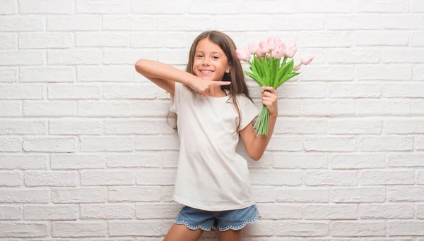 手と指で指している非常に幸せな母の日に花を持って白いレンガ壁にヒスパニック系の子供 — ストック写真