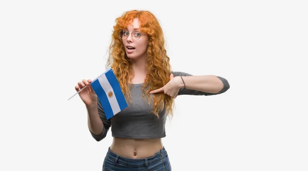 Młoda Ruda Kobieta Trzyma Flagę Argentyny Niespodzianka Twarzy Palcem Wskazującym — Zdjęcie stockowe
