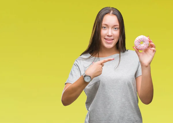 非常に幸せな手と指で指している分離の背景に甘いドーナツを食べる若い白人女性 — ストック写真
