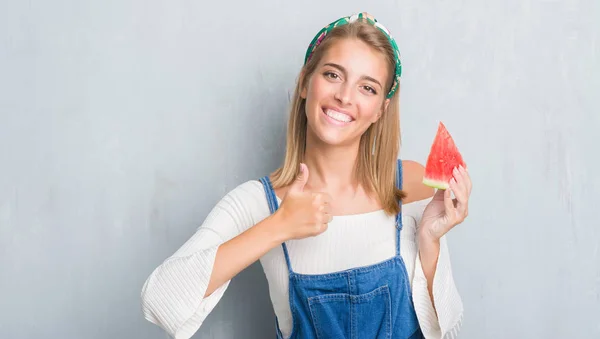 グランジに美しい若い女性灰色壁笑顔の サイン 優秀な兆候を親指をやって幸せなスイカを食べる — ストック写真