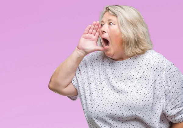 Senior plus size caucasian woman over isolated background shouting and screaming loud to side with hand on mouth. Communication concept.