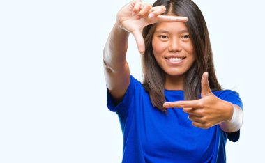 Genç Asyalı kadın elle yapma çerçeve ve parmakları ile mutlu yüz gülümseyen izole arka plan üzerinde. Yaratıcılık ve Fotoğrafçılık kavramı.